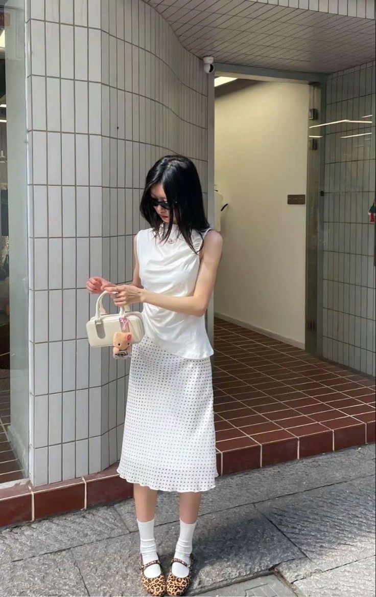 Woman in a white top and polka dot skirt holding a small handbag outdoors
