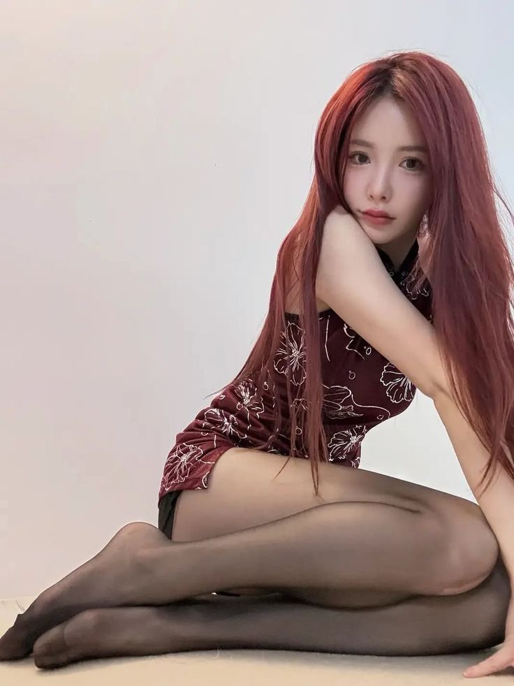 Woman with long red hair in a cheongsam dress and black pantyhose posing indoors