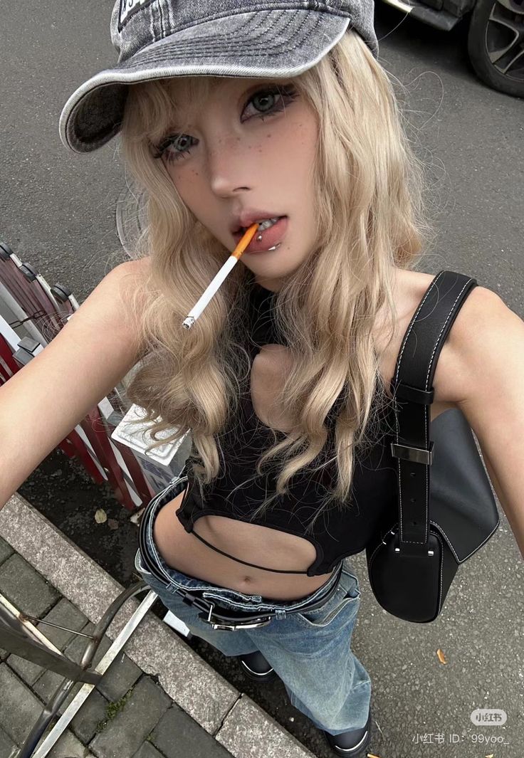 Blonde woman in a crop top and jeans holding a cigarette in her mouth