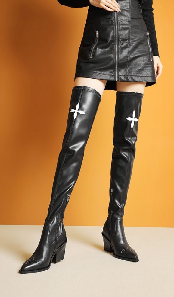 Person wearing a black leather skirt and thigh-high boots with white embroidery