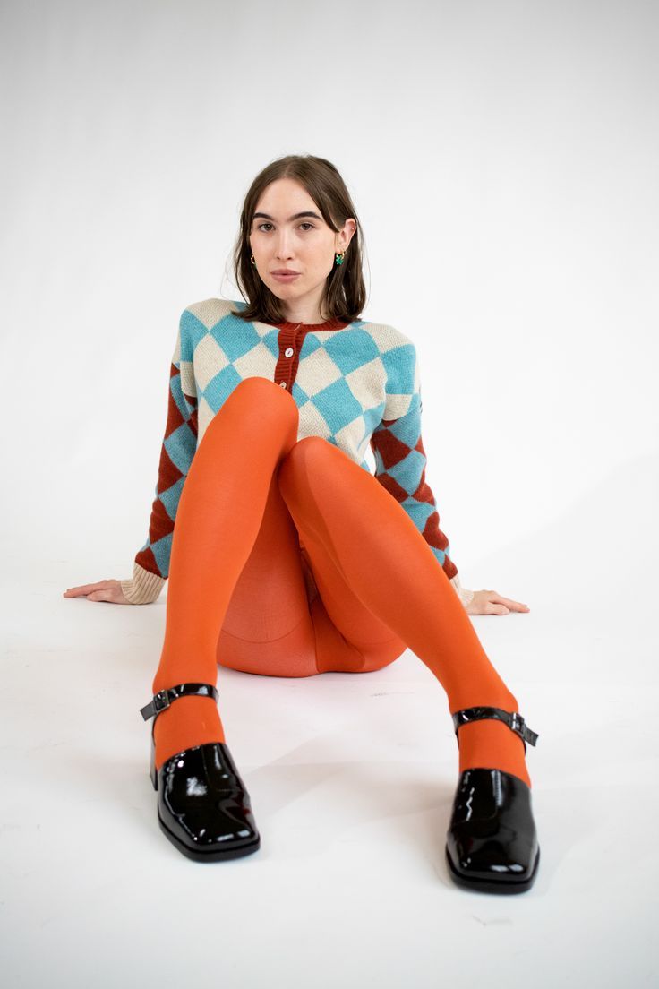 Woman in an argyle cardigan and orange tights sitting on a white background