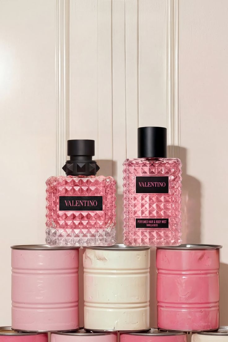 Two Valentino perfume bottles with pink liquid on stacked pink and white cans