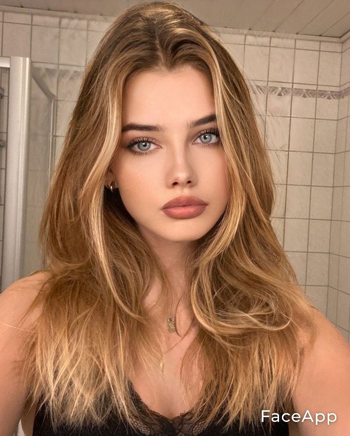 Woman with long blonde hair and blue eyes wearing a black top indoors