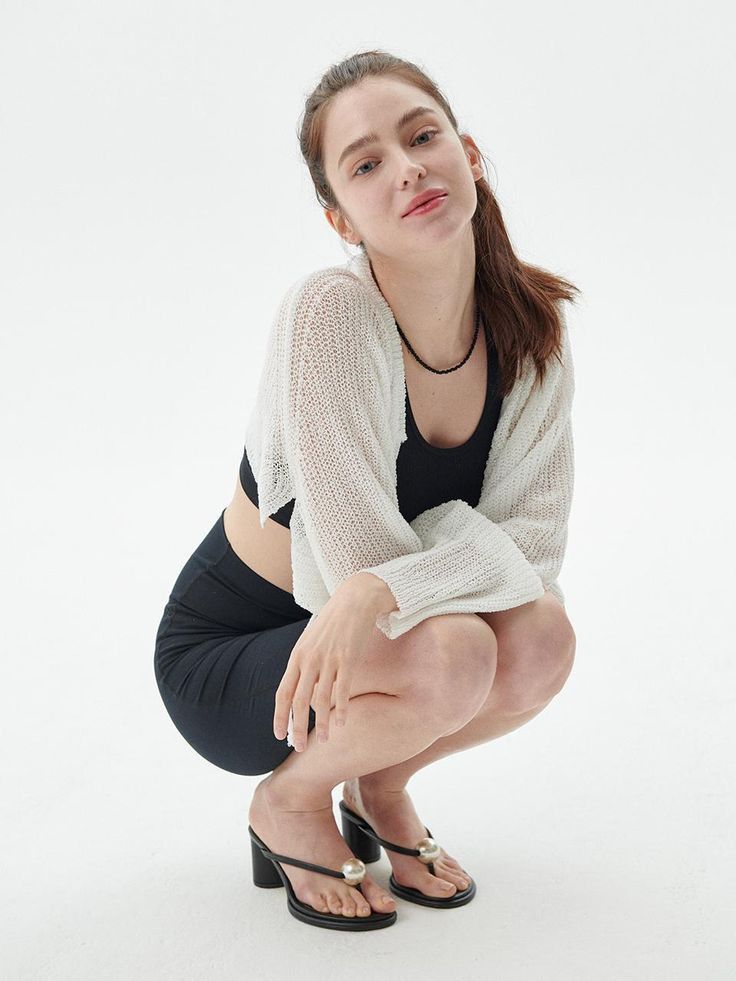 Woman in a white cardigan and black crop top squatting in a studio