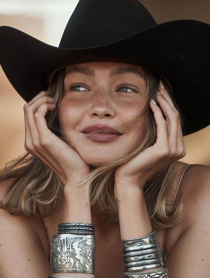 Woman with freckles and a cowboy hat, wearing silver bracelets, looking away