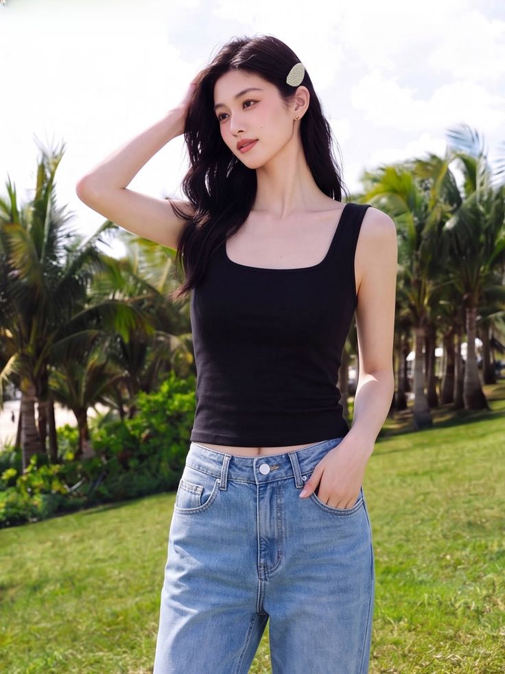 Woman in a black tank top and blue jeans outdoors with palm trees