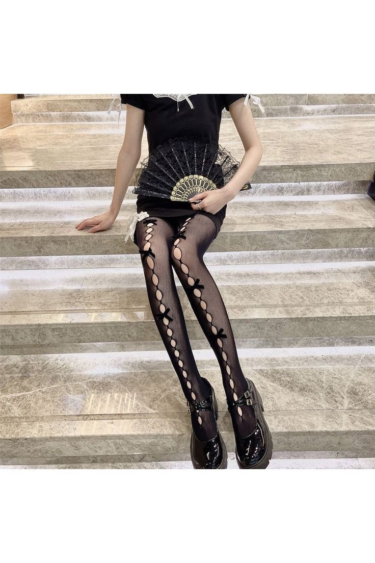 Person in a black dress and fishnet stockings holding a lace fan while sitting on stairs