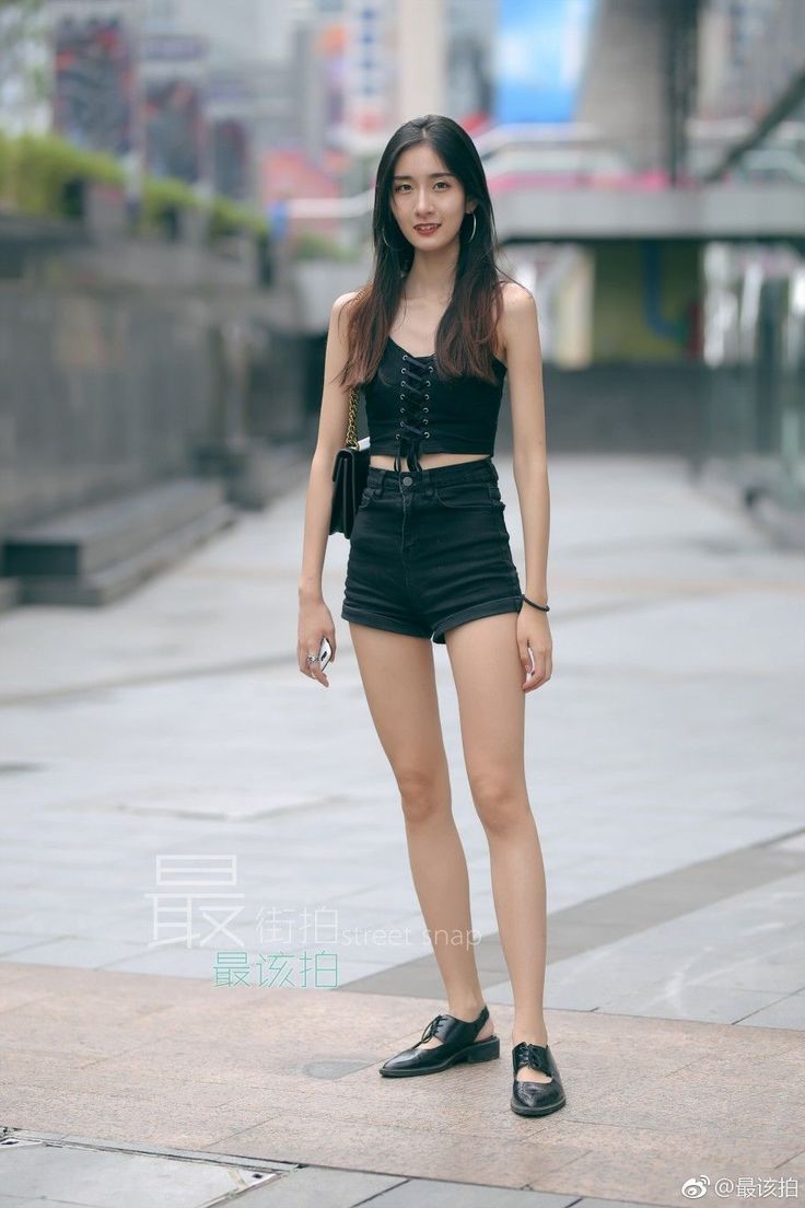 Woman in a black crop top and denim shorts standing on a street