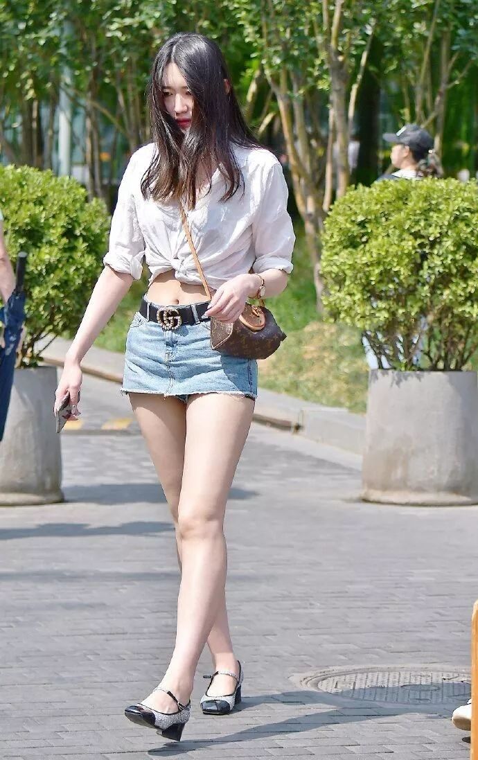 Woman in a white knotted shirt and denim mini skirt walking outdoors