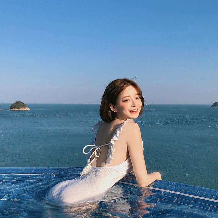 Woman in a white swimsuit in an infinity pool overlooking the ocean