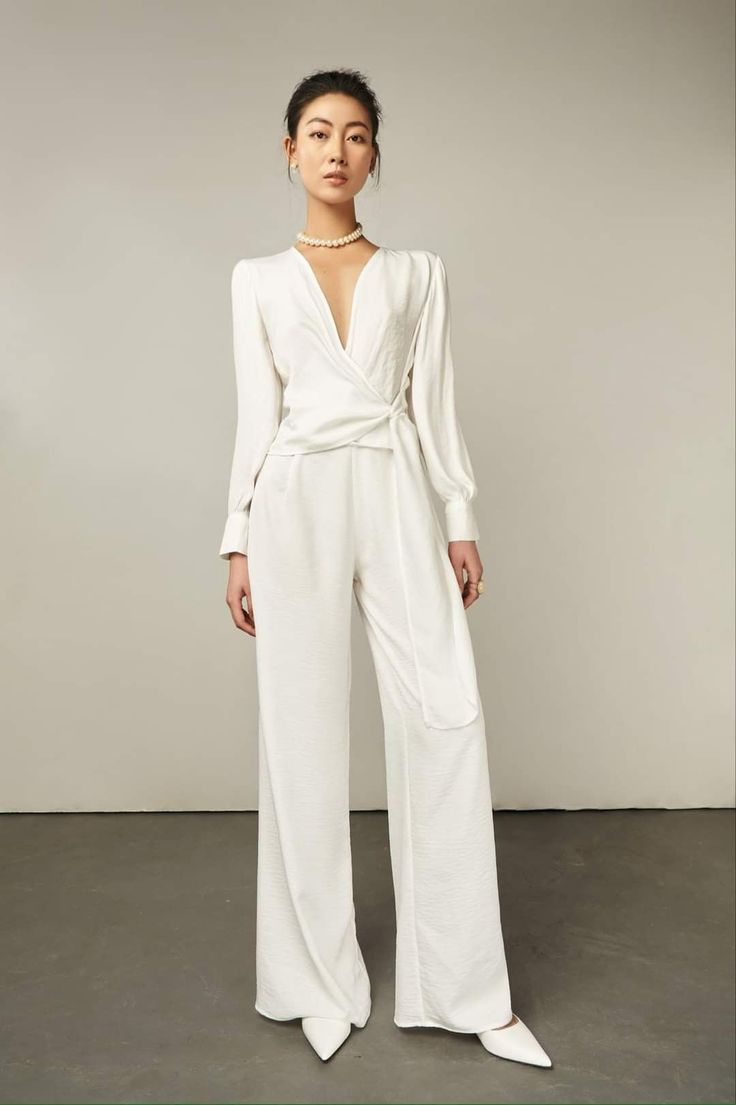Woman in a white jumpsuit with a pearl necklace posing in a studio