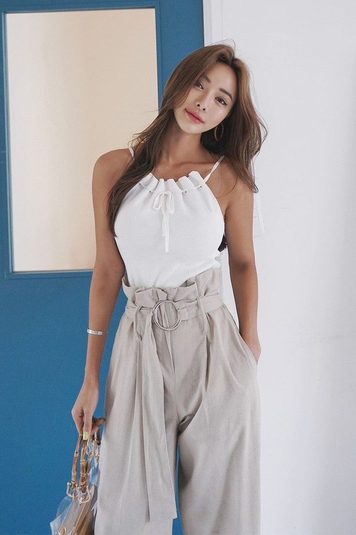 Woman with long hair wearing a white top and high-waisted wide-leg pants indoors