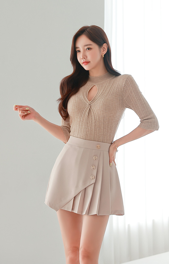 Woman in a beige ribbed top and mini skirt posing indoors