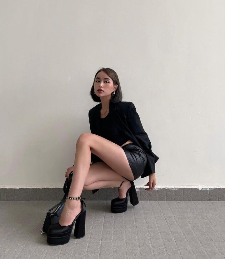 Woman in a black blazer and leather skirt squatting indoors
