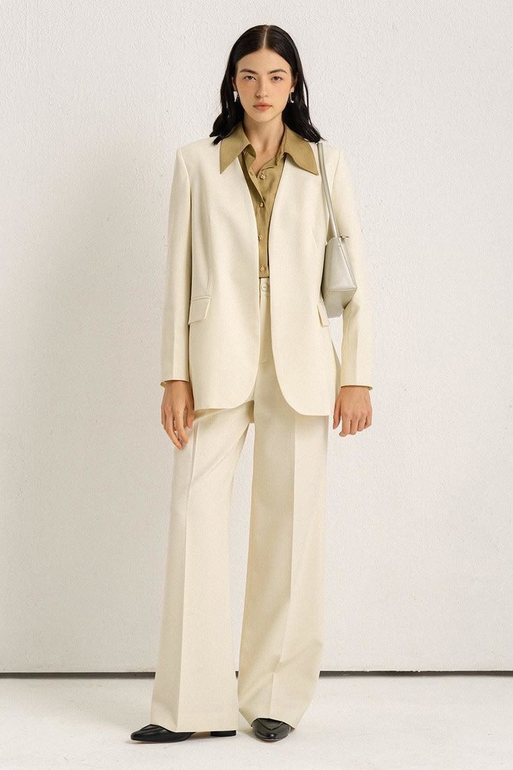 Woman in a cream suit and olive shirt posing indoors