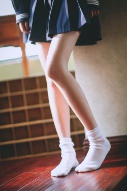 Person in a school uniform and white socks standing on a wooden floor