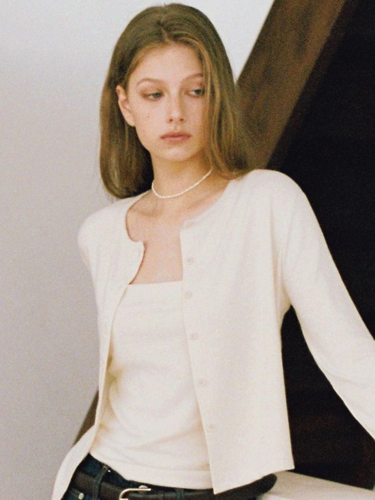 Young woman with long hair wearing a white cardigan and pearl necklace