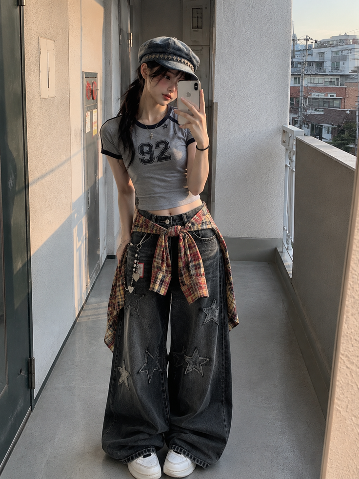 Woman in a crop top and wide leg jeans taking a mirror selfie outdoors