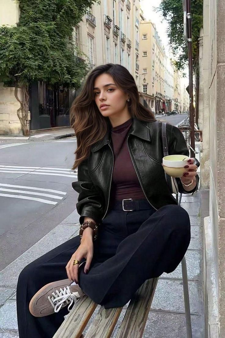 Woman with long hair in a leather jacket sitting on a bench on a city street