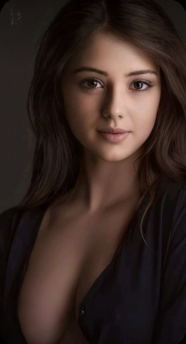 Woman with long dark hair and exposed cleavage in soft lighting