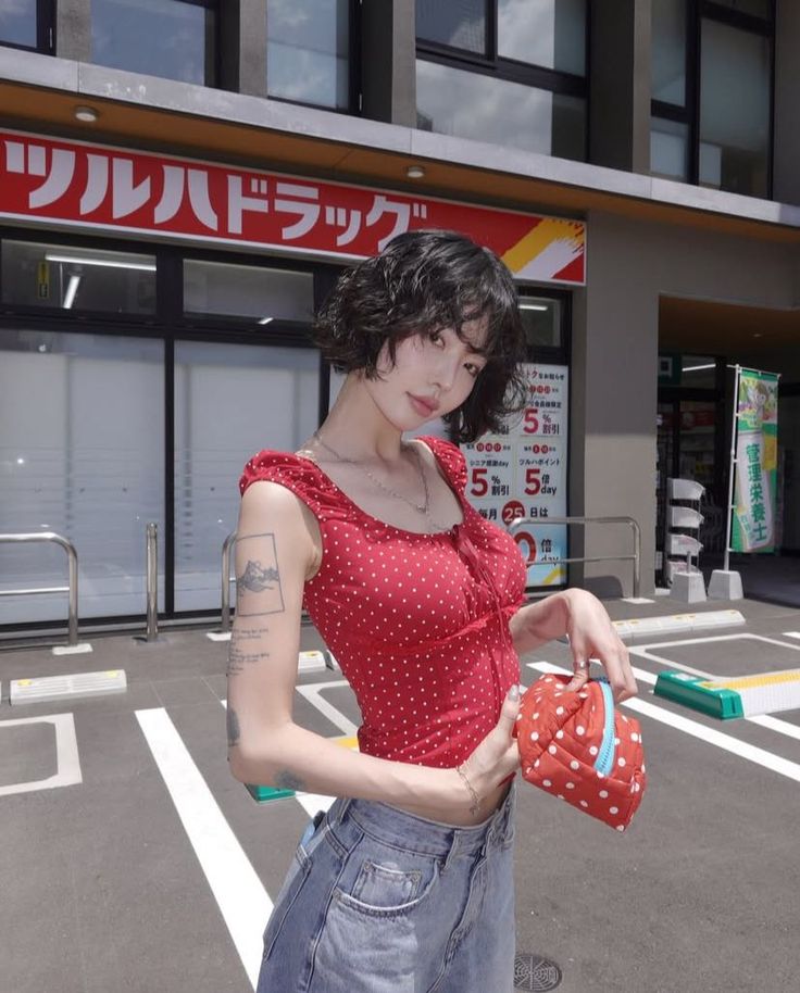 Woman with short dark hair in a red polka dot top and denim jeans outdoors