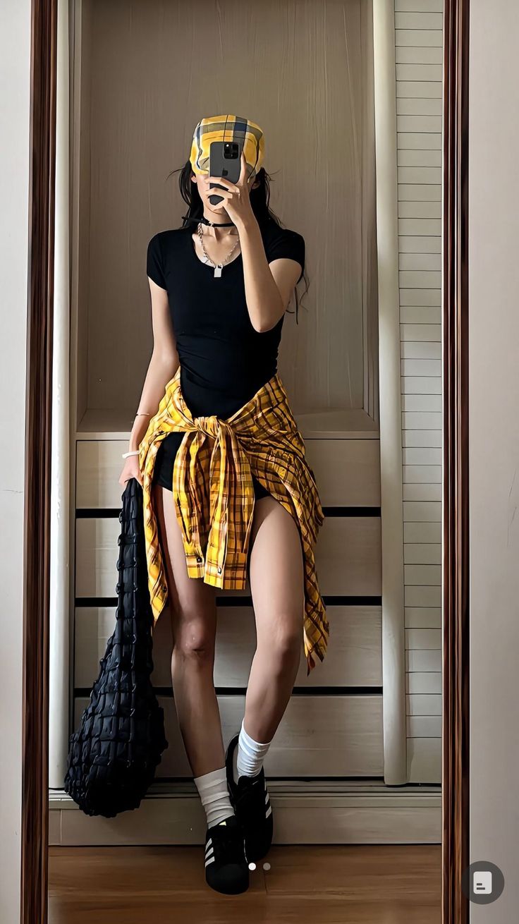 Person in a black top and plaid shirt tied around the waist taking a mirror selfie