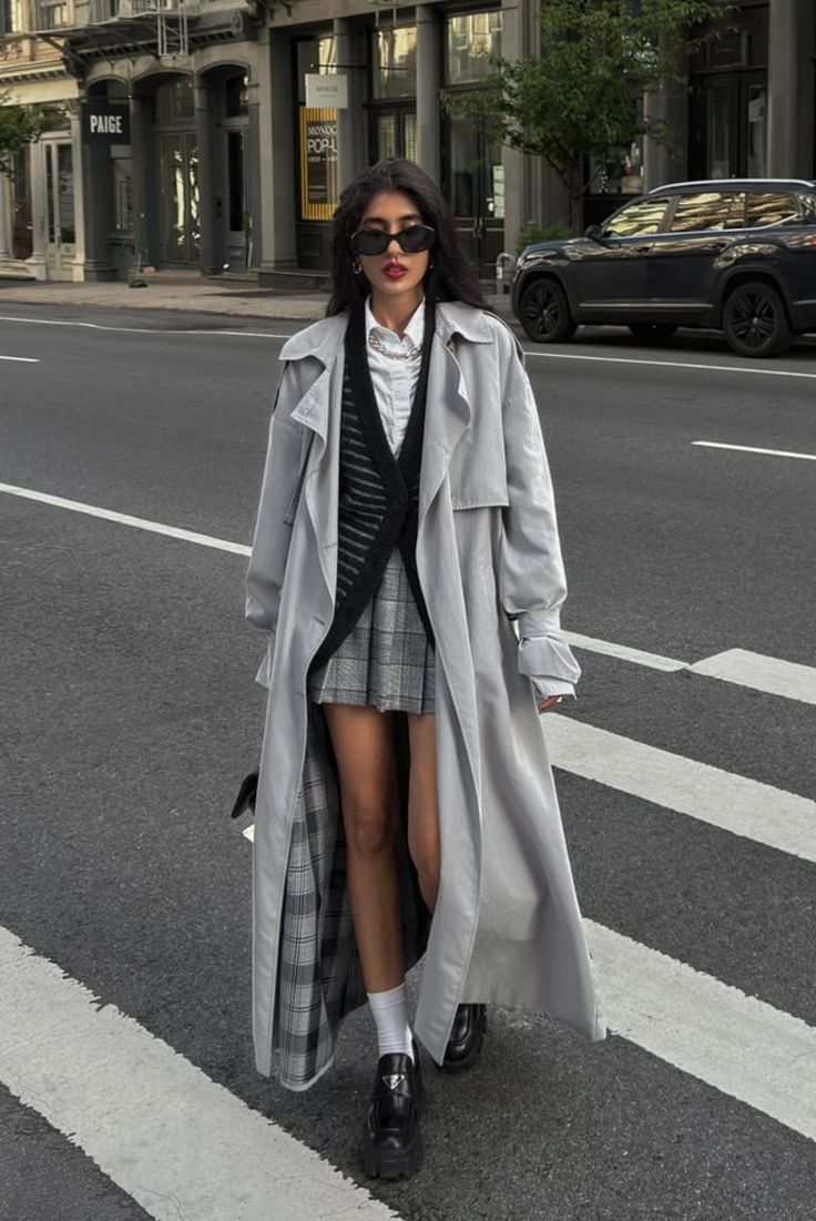 Woman in a long trench coat and plaid skirt walking on a city street