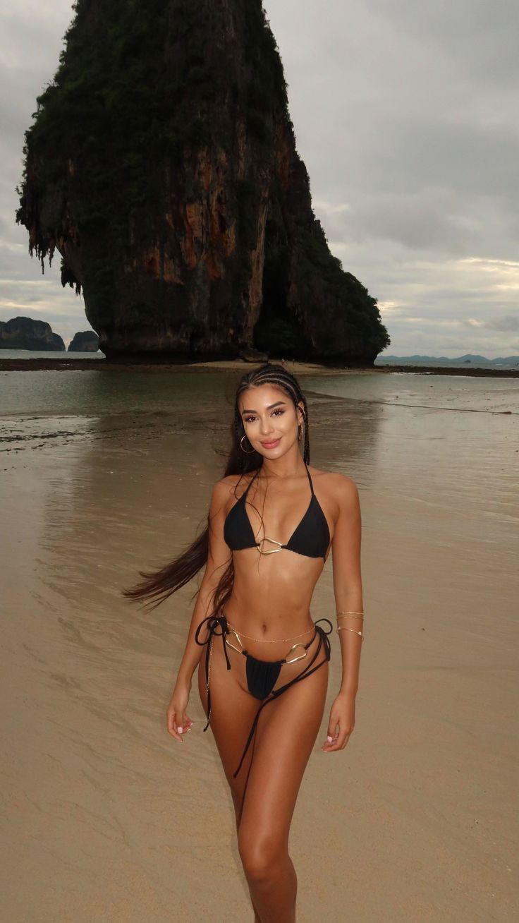 Woman in a black bikini with gold accents on a beach with large rock formations