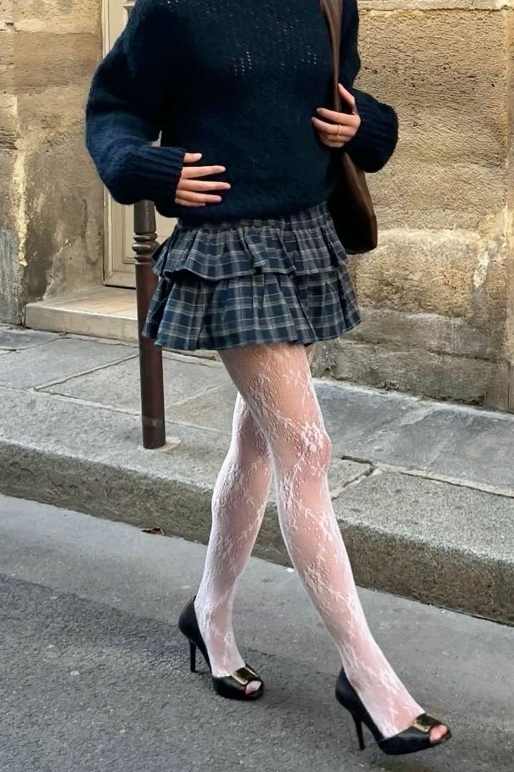 Person in a plaid skirt, white lace tights, and black sweater walking on a street