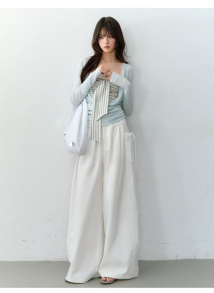 Woman with long hair wearing a light blue top and white wide-leg pants indoors