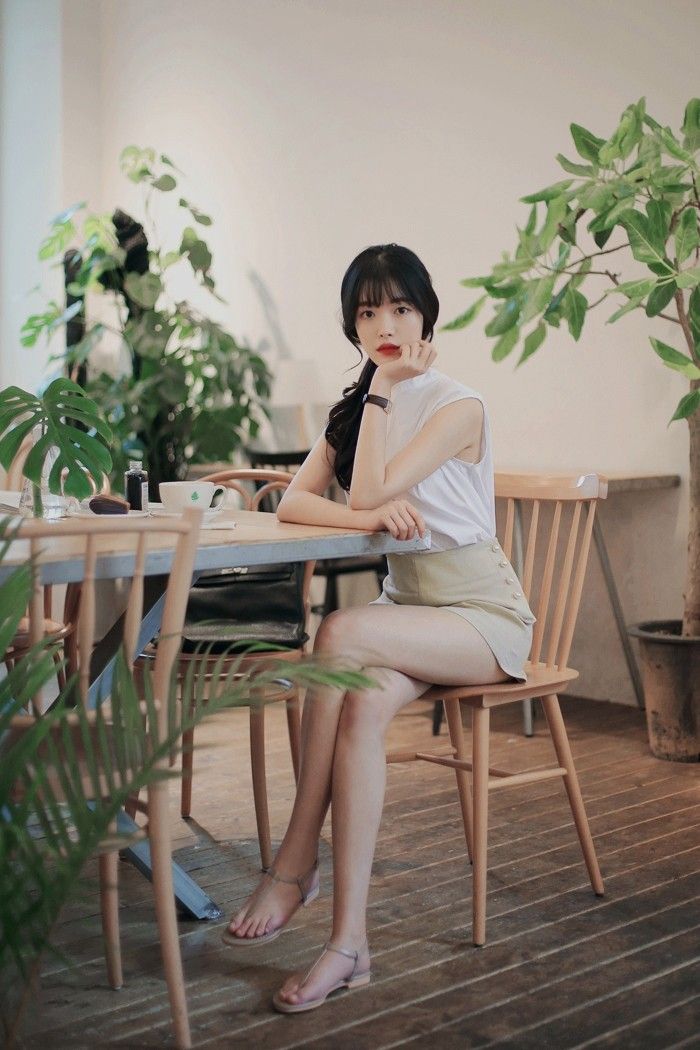 Woman with a ponytail sitting at a table in a cafe with plants