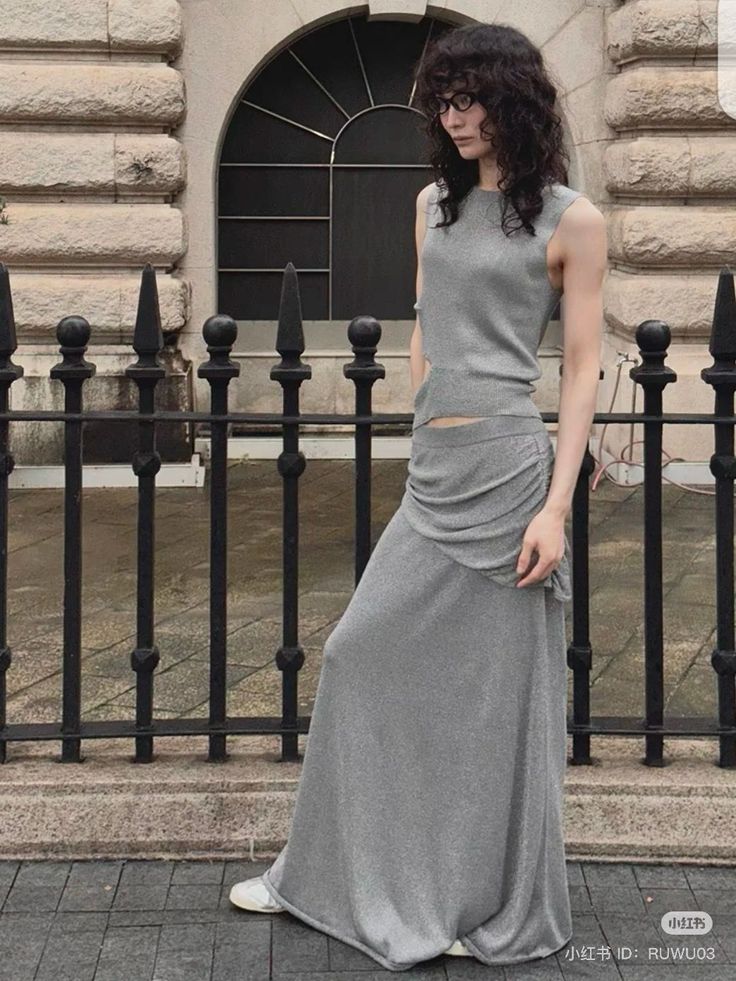 Person with curly hair and glasses wearing a gray two-piece outfit outdoors