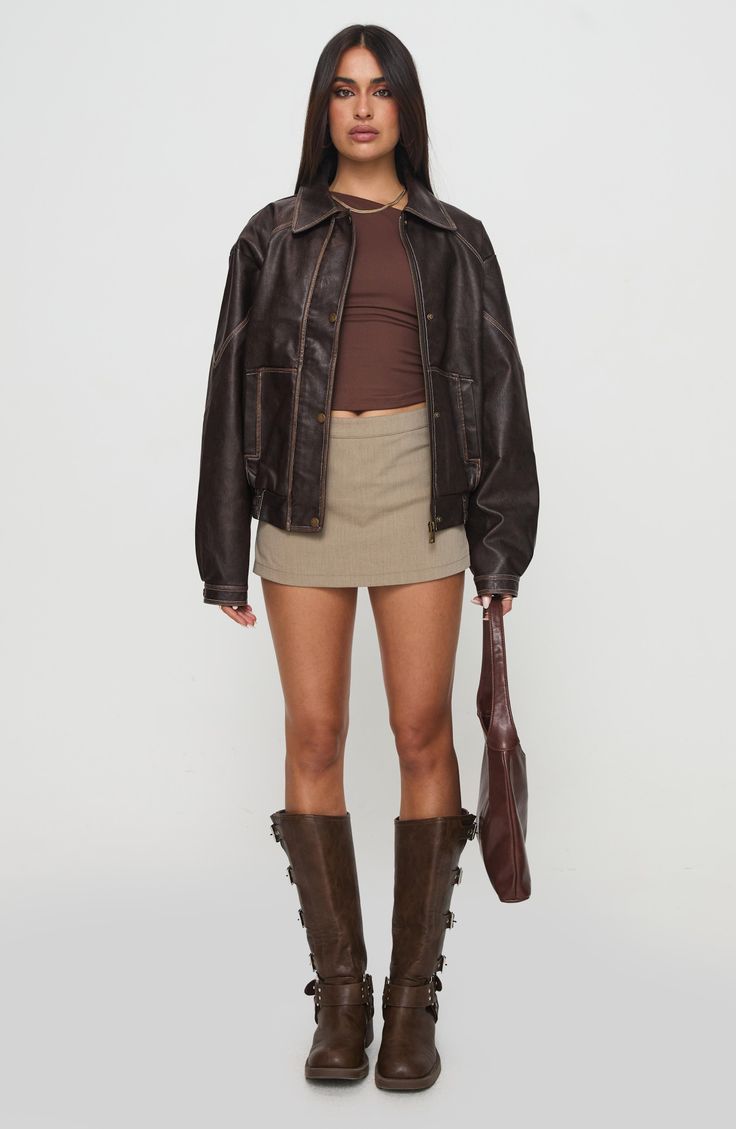 Woman in a brown leather jacket, mini skirt, and knee-high boots holding a handbag
