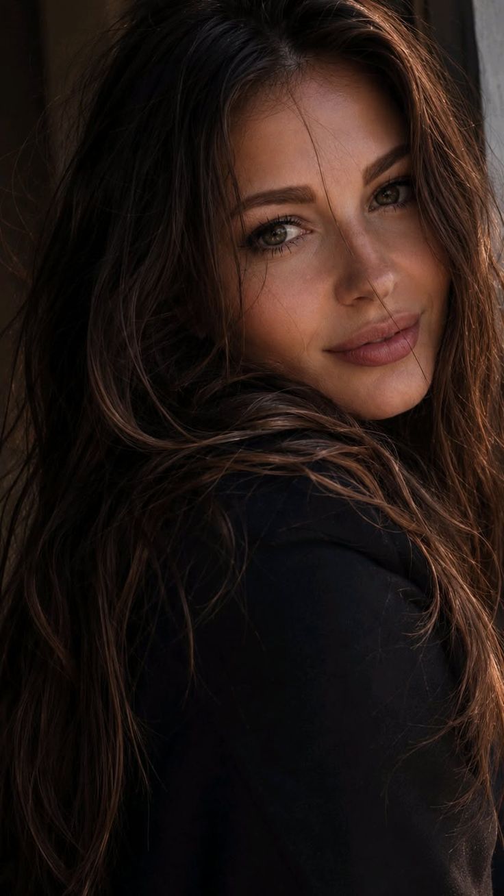 Woman with long dark hair wearing a black top, looking over her shoulder