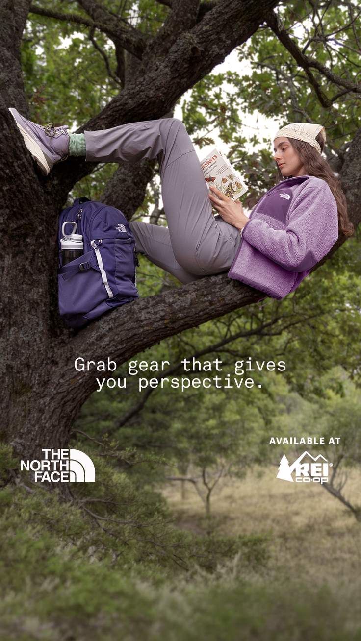 Woman in hiking gear reading a book while sitting on a tree branch