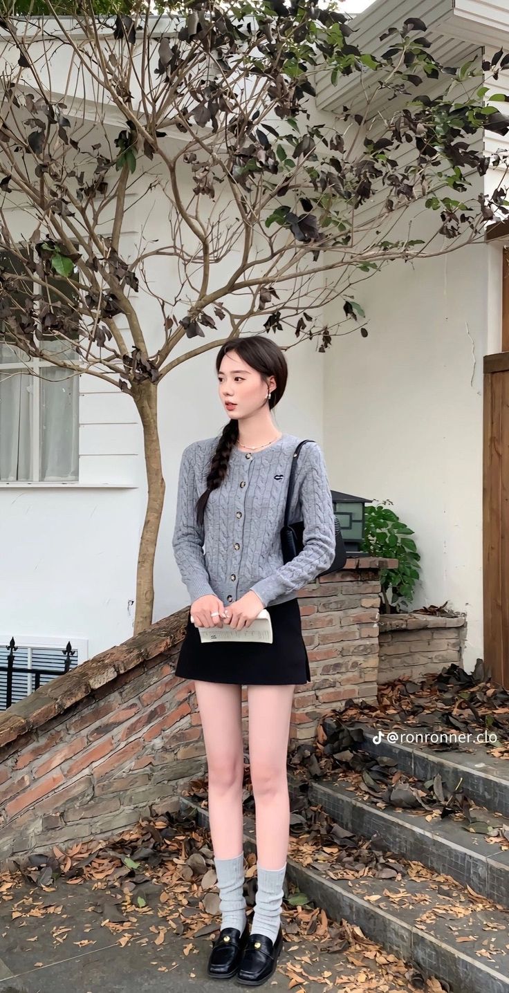 Woman with a braid wearing a gray cardigan and black mini skirt outdoors