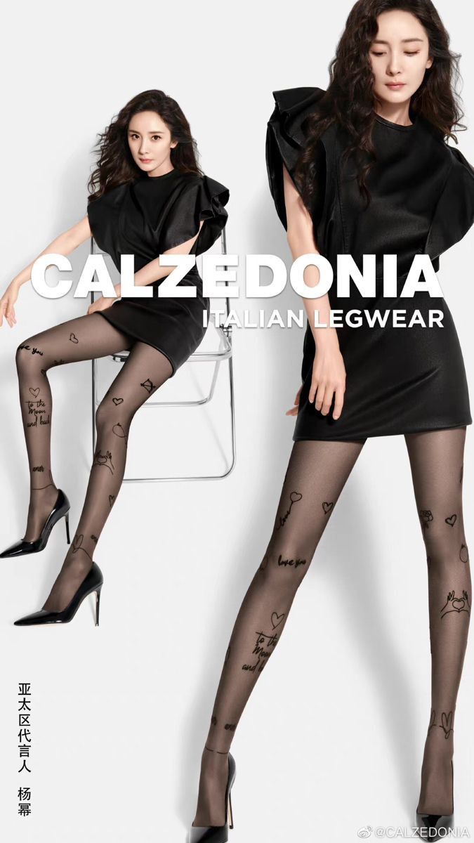 Two women in black dresses and patterned tights posing in a studio