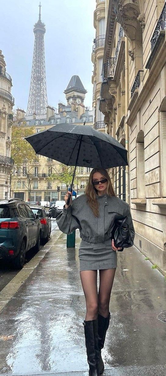Woman in a grey outfit holding an umbrella on a rainy street with the Eiffel Tower in the background