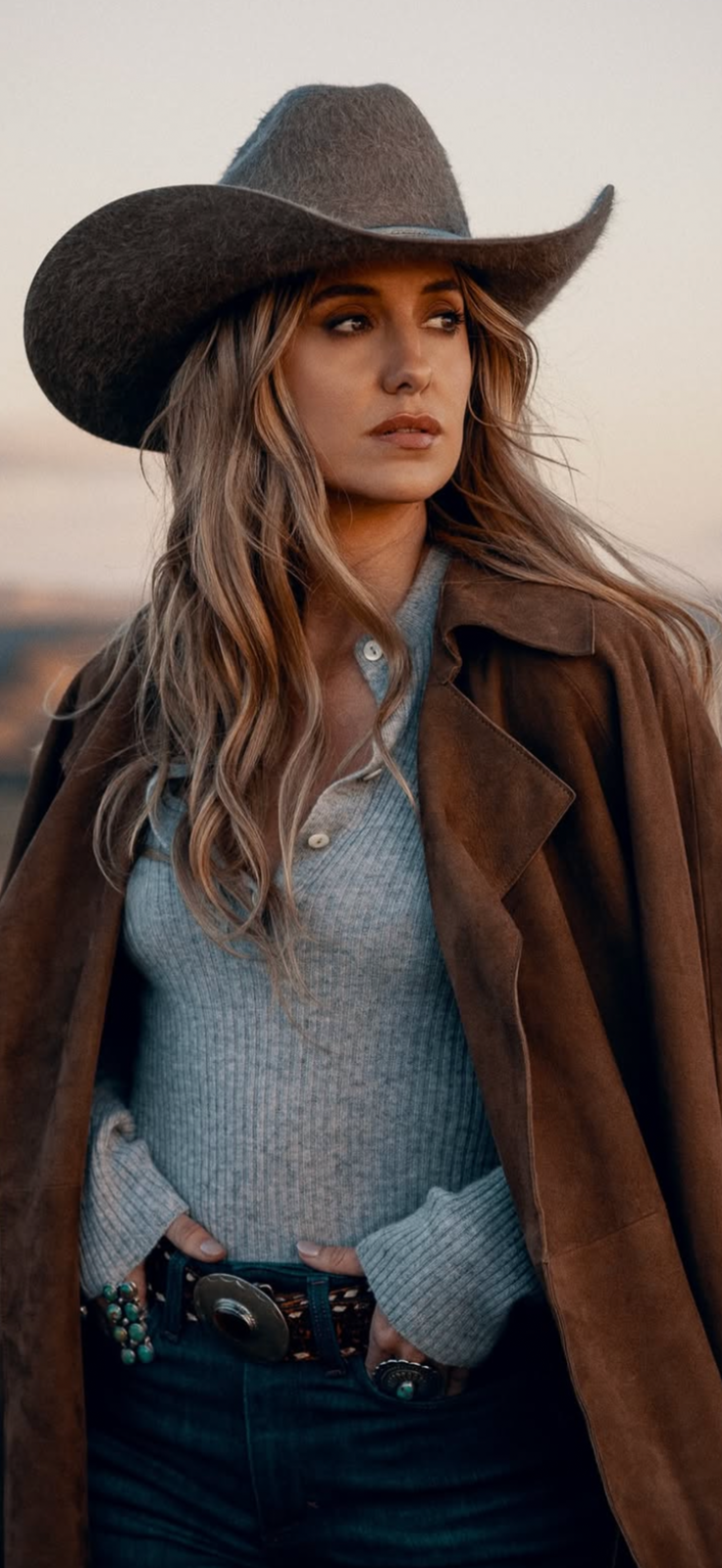 Woman in a cowboy hat and brown coat with a western belt at golden hour