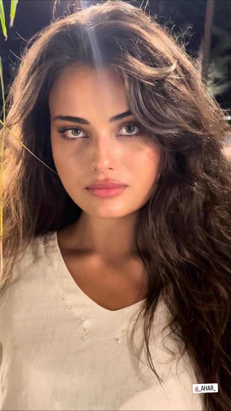 Woman with long dark hair wearing a white shirt, looking directly at the camera