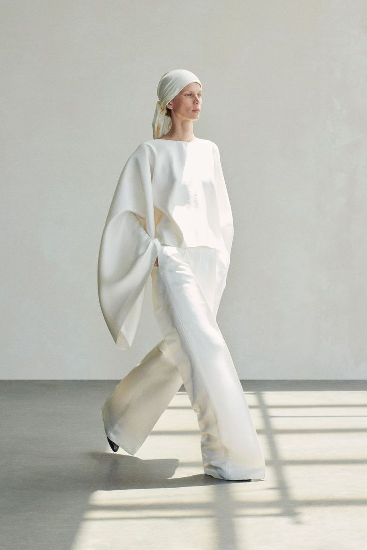 Woman in a white oversized outfit and head scarf walking indoors