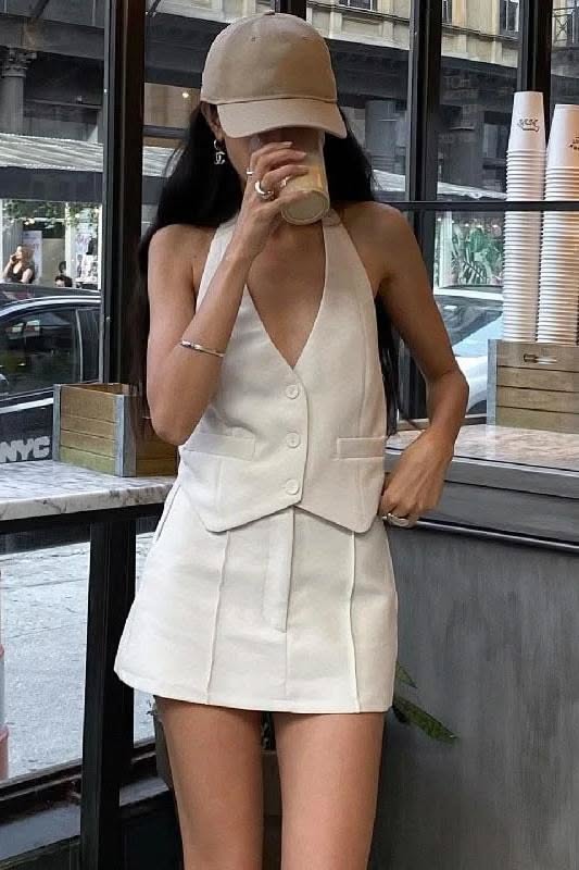 Woman in a white sleeveless top and mini skirt drinking from a cup indoors