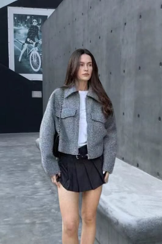 Woman in a gray cropped jacket and black pleated skirt outdoors