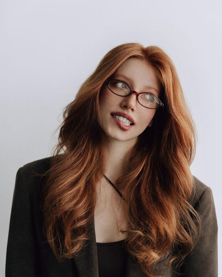 Woman with long red hair and glasses biting her lip, looking to the side