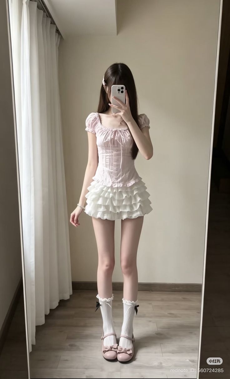 Person in a pink top and white ruffle skirt taking a mirror selfie