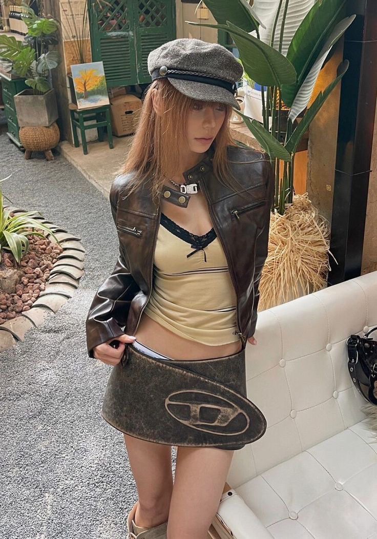Woman in a brown leather jacket and mini skirt with a newsboy cap outdoors