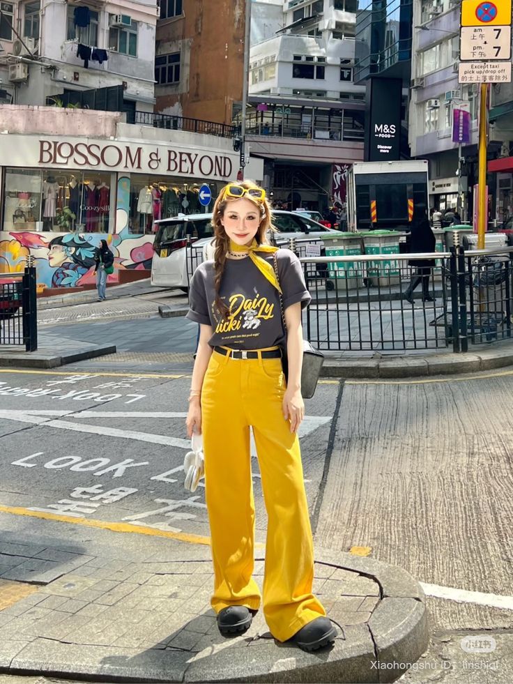 Woman in yellow pants and a gray t-shirt posing on a city street