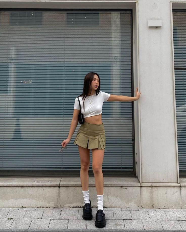 Woman in a white crop top and green pleated skirt standing outdoors