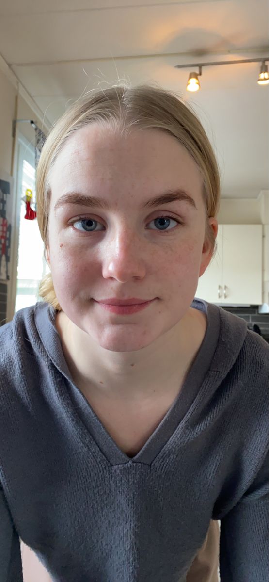 Young woman with blonde hair and blue eyes wearing a grey hoodie indoors