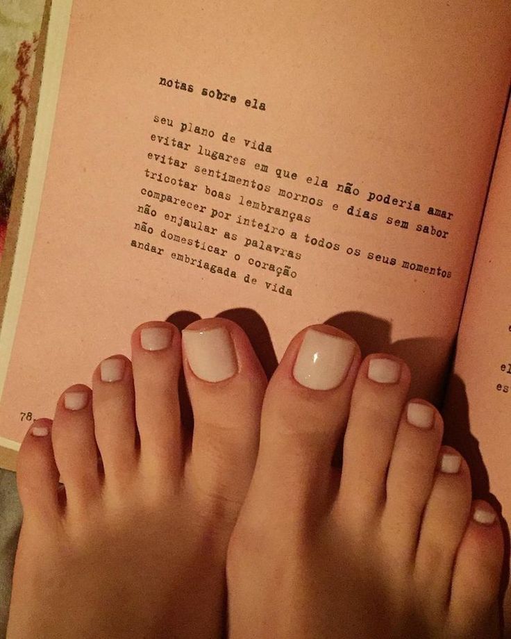 Feet with light pink nail polish resting on an open book with text